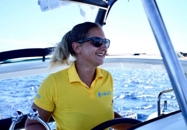 Skipperin Sasi steuert ein Segelboot im Sailwithus-T-Shirt