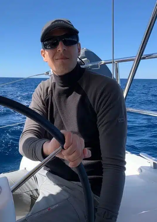 Skipper Thomas steuert ein Segelboot im Sailwithus-T-Shirt