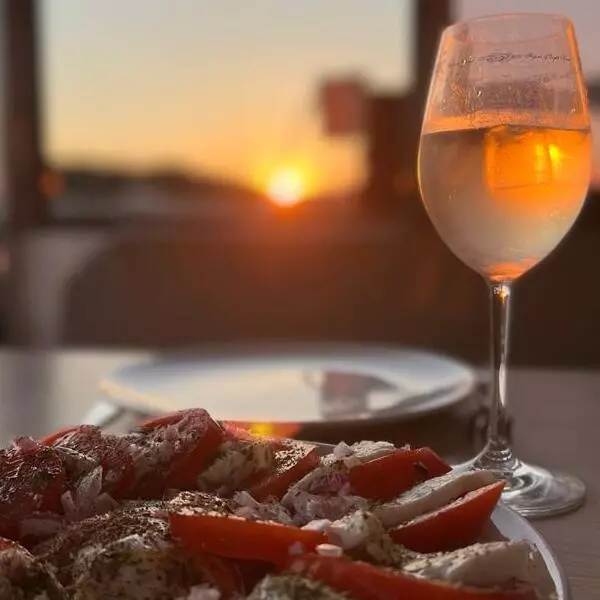 Ein gedeckter Tisch mit einer Schale geschnittener Tomaten und Mozzarella, dazu ein Glas Roséwein, mit einem Sonnenuntergang im Hintergrund während eines Segelurlaubs.