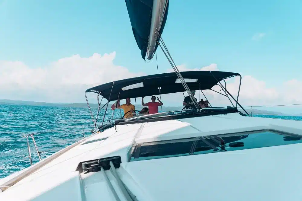 Ein Blick vom Bug einer Segelyacht. Er zeigt mehrere Personen, die einen sonnigen Tag auf See genießen, umgeben von blauem Himmel und Wasser.