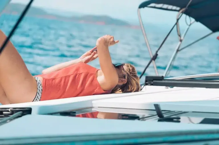 Eine Frau entspannt sich auf dem Deck eines Segelboots, sonnt sich und schützt ihre Augen mit der Hand, umgeben vom offenen Wasser.