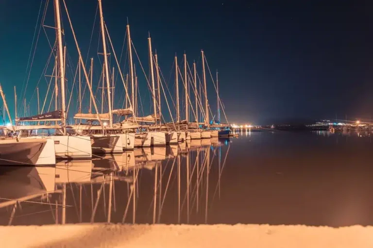 Nachtansicht eines ruhigen Yachthafens mit mehreren nebeneinander angedockten Segelyachten, die sich unter einem Sternenhimmel im Wasser spiegeln.
