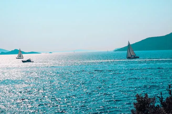 Segelurlaub: Gleiten Sie über ein glitzernd blaues Meer, eingerahmt von fernen Hügeln unter einem klaren Himmel.