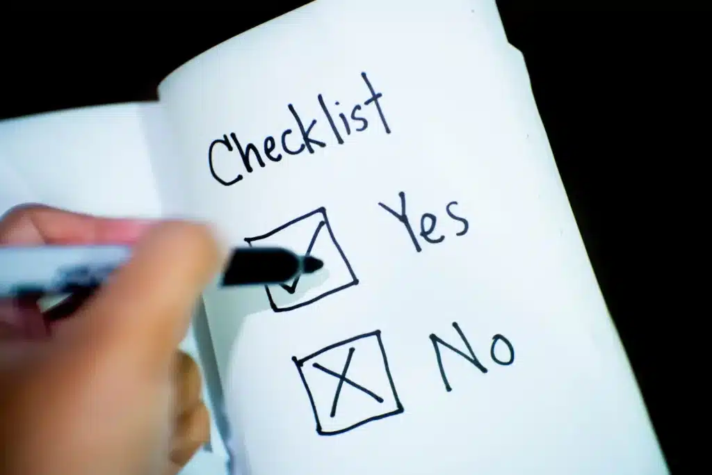 Die Hand einer Person hält während einer Segelreise einen Stift und markiert auf einem Notizbuch vor einem schwarzen Hintergrund „Ja“ auf einer Checkliste, wobei die Optionen „Ja“ und „Nein“ hervorgehoben sind.