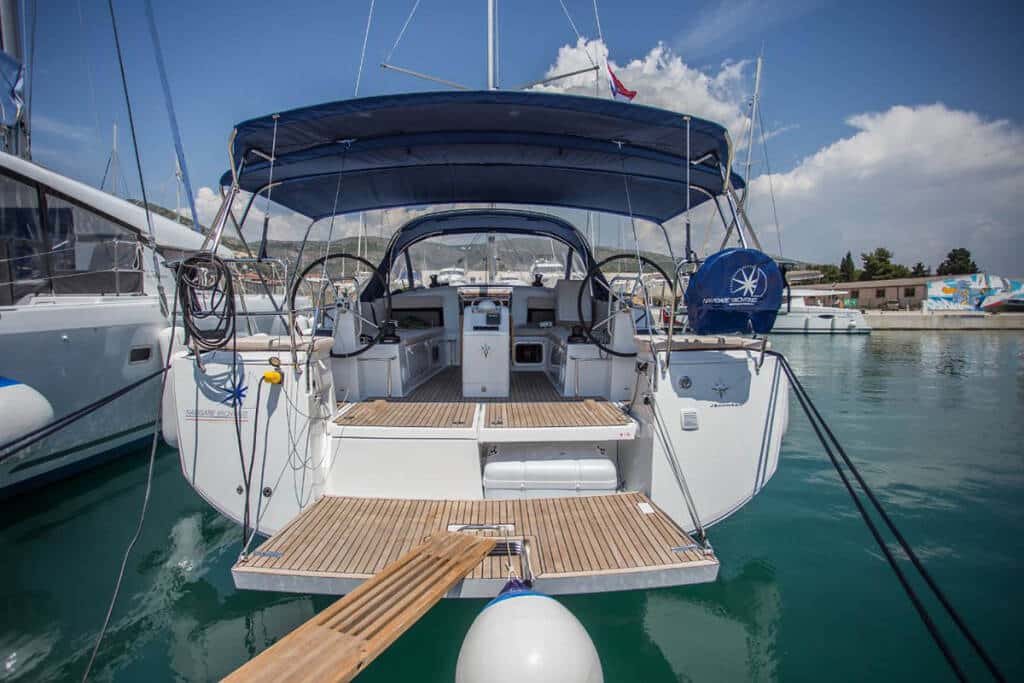 Ein Luxus-Katamaran, der in einem Yachthafen vor Anker liegt, mit klarem Himmel über ihm, mit geräumigem Achterdeck und zwei Steuerrädern, umgeben von anderen Booten.