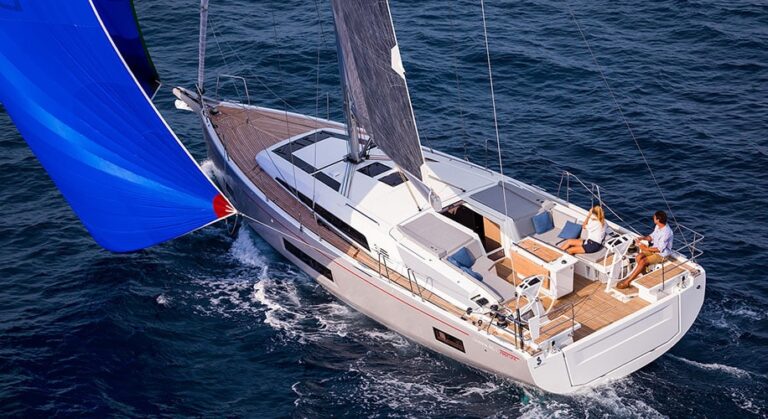 Ein modernes Segelboot mit blauem Spinnaker-Segel gleitet während eines Segeltörns über den Ozean. An Deck sind zwei Personen zu sehen, die die Fahrt genießen.
