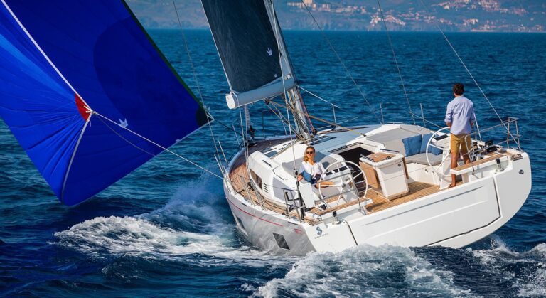 Ein Segelboot mit blauen Segeln gleitet über das Wasser, gesteuert von zwei Personen an einem klaren Tag mit entfernten Hügeln im Hintergrund während eines Segeltörns.