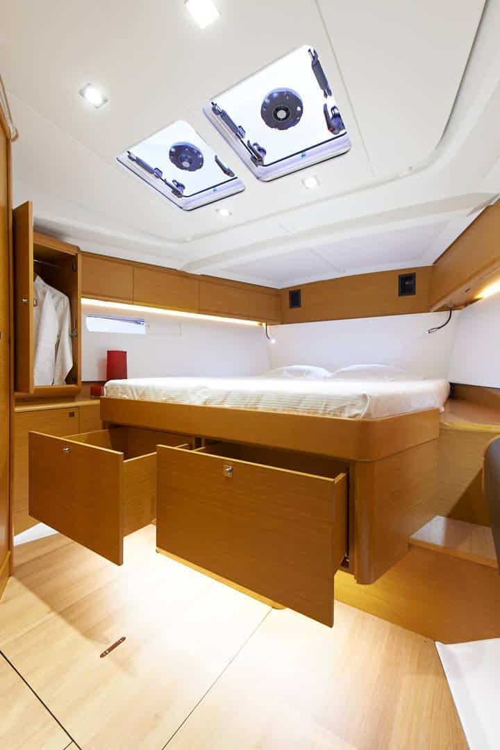 Innenansicht einer Segelyachtkabine mit großem Bett, Holzschränken und Oberlichtfenstern für natürliches Licht. Hell und elegant eingerichtet mit einem einheitlichen Farbschema.
