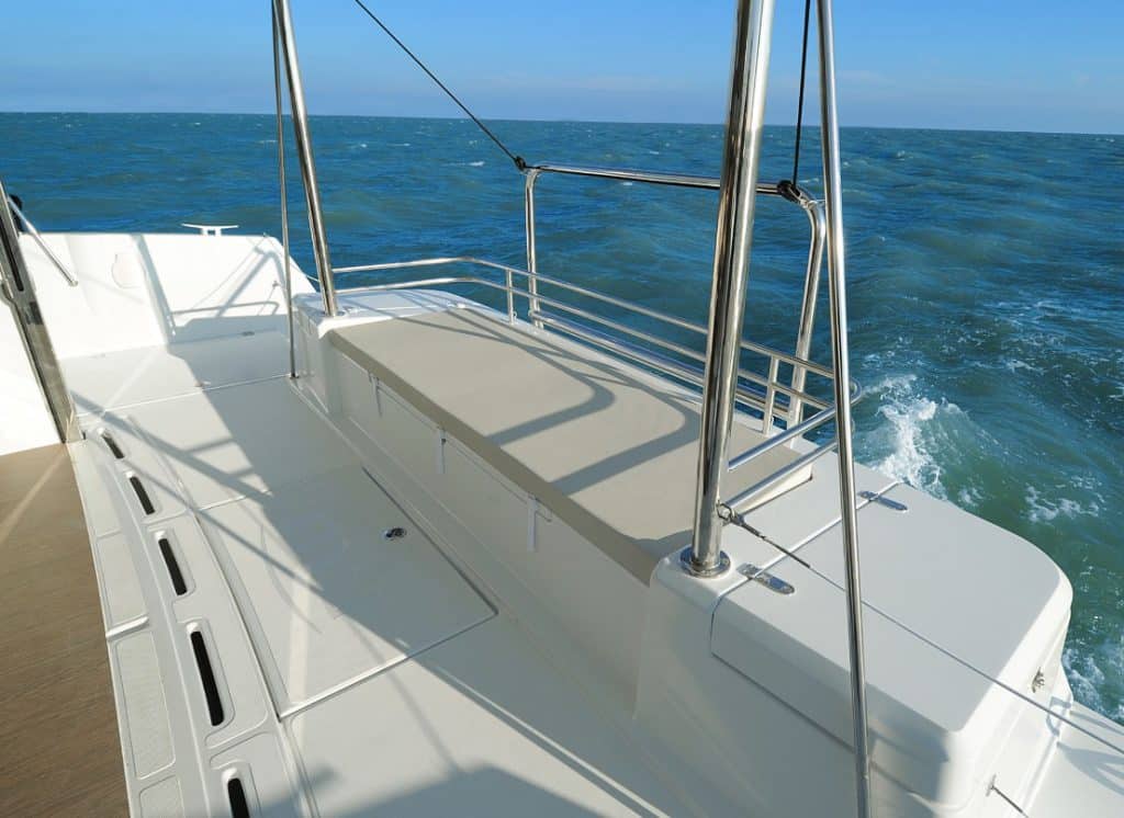 Eine Segelyacht kreuzt auf dem Ozean, vom Achterdeck aus betrachtet, mit Blick auf die Reling und das Meer im Hintergrund unter einem klaren Himmel.