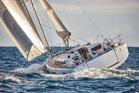 Eine Segelyacht mit gesetzten Segeln navigiert durch das unruhige blaue Meer und bietet einen klaren Himmel und ein dynamisches Wellenspiel rund um das Schiff.