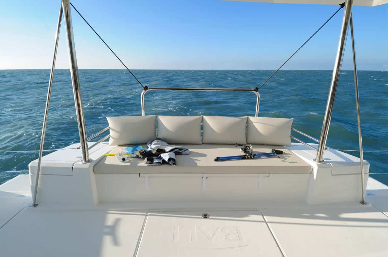 Rückansicht einer Segelyacht mit gepolsterten Sitzen und Angelausrüstung auf einem ruhigen blauen Meer unter einem klaren Himmel.