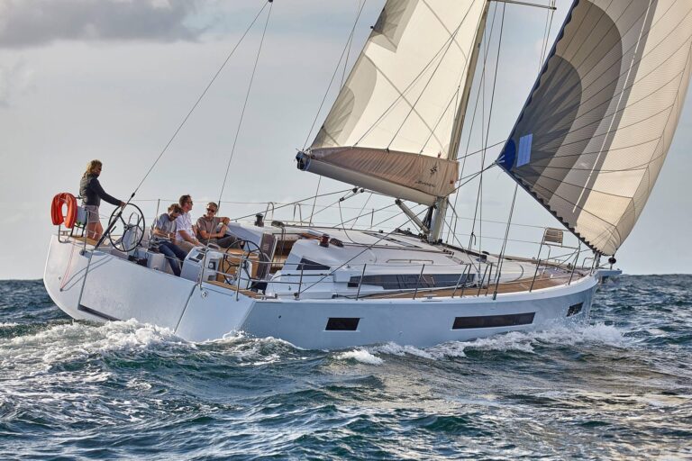 Eine Gruppe von Menschen segelt auf einer modernen Segelyacht mit voll ausgefahrenen Segeln durch unruhiges Meer unter einem bewölkten Himmel.