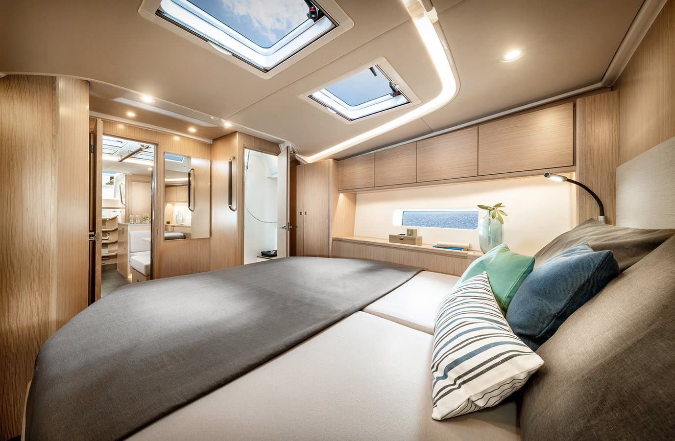 Luxuriöses Yachtschlafzimmer mit großem Bett mit blauen und grünen Kissen, Holzvertäfelung, eleganten Schränken und stimmungsvoller Beleuchtung. Zwei Oberlichter füllen den Raum während Ihres Segeltörns mit natürlichem Licht.