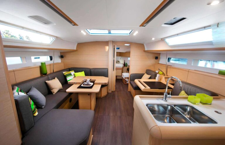 Innenansicht eines modernen, geräumigen Wohnmobils mit elegantem Küchenbereich, bequemen Essbereichen mit grauen Kissen, hellgrünen Akzenten, die an die leuchtenden Farben eines Katamarans erinnern, und reichlich Tageslicht.