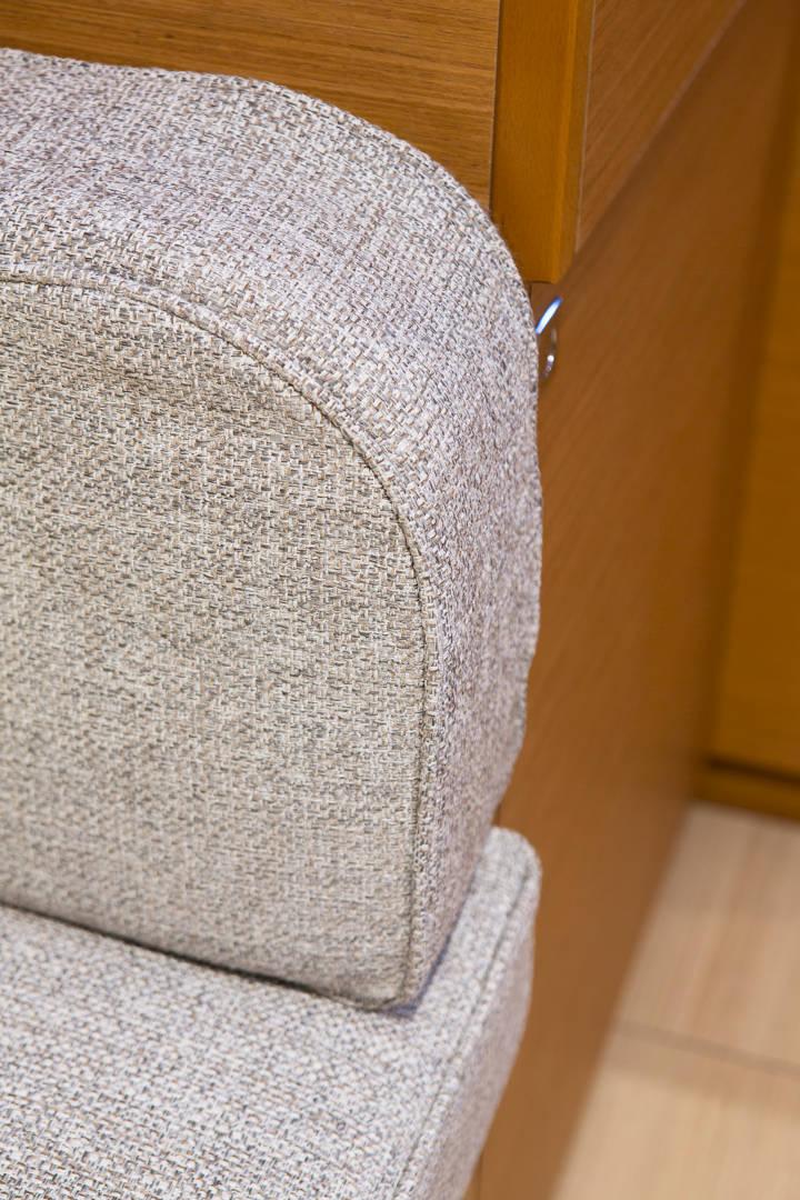 Nahaufnahme eines beigefarbenen Polsterstuhls mit abgerundeter Armlehne neben einem Holzschrank in einem Wohnhaus.