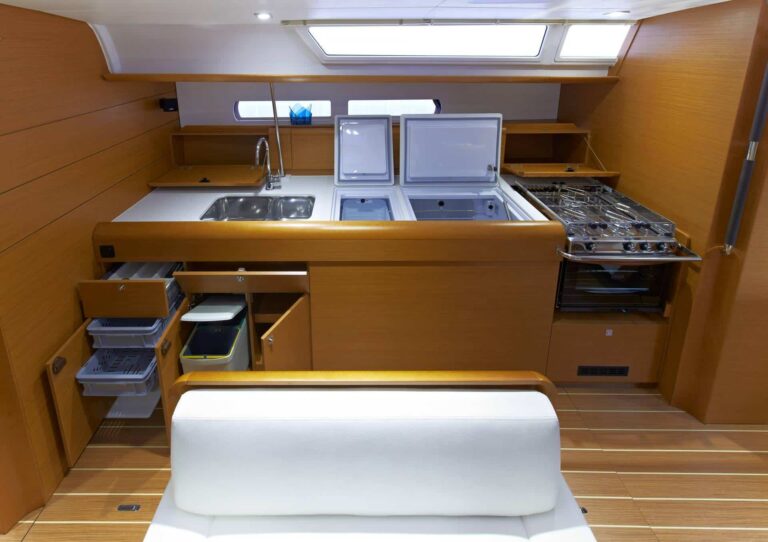 Eine moderne Bootsküche auf einer eleganten Segelyacht mit Holzschränken, einer Edelstahlspüle, einer organisierten Theke mit offenen Deckeln, die Staufächer freigeben, einem Herd und einem Ofen auf der rechten Seite sowie eingebauten Schubladen und Regalen. Ein Oberlicht sorgt für natürliches Licht im Raum, perfekt für jede Segelreise.