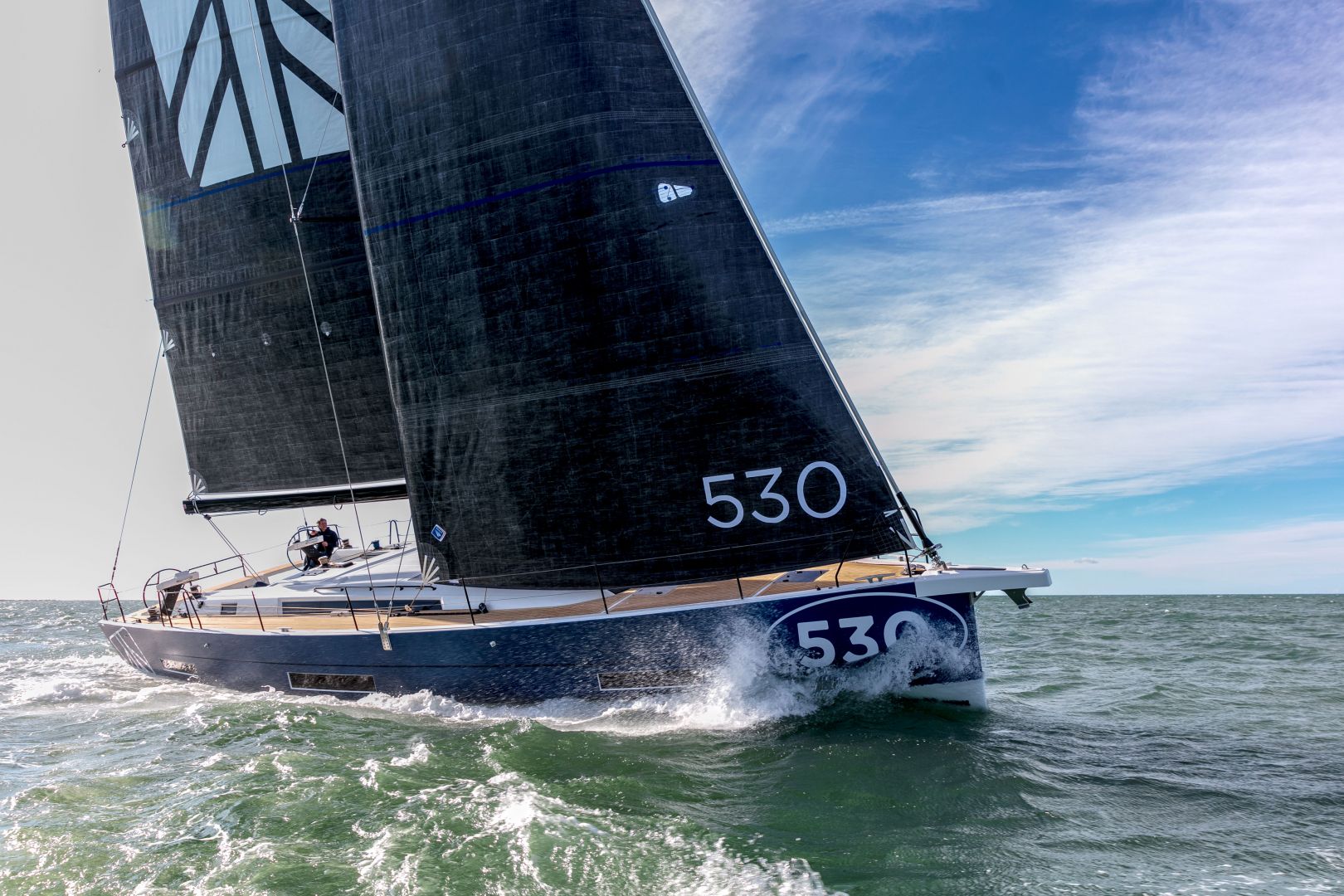 Ein elegantes schwarzes Segelboot mit der Nummer 530 auf Segel und Rumpf gleitet schnell durch den Ozean. Der klare blaue Himmel und die sanften Wellen bilden eine malerische Kulisse, perfekt für ein unvergessliches Yachtcharter-Erlebnis.
