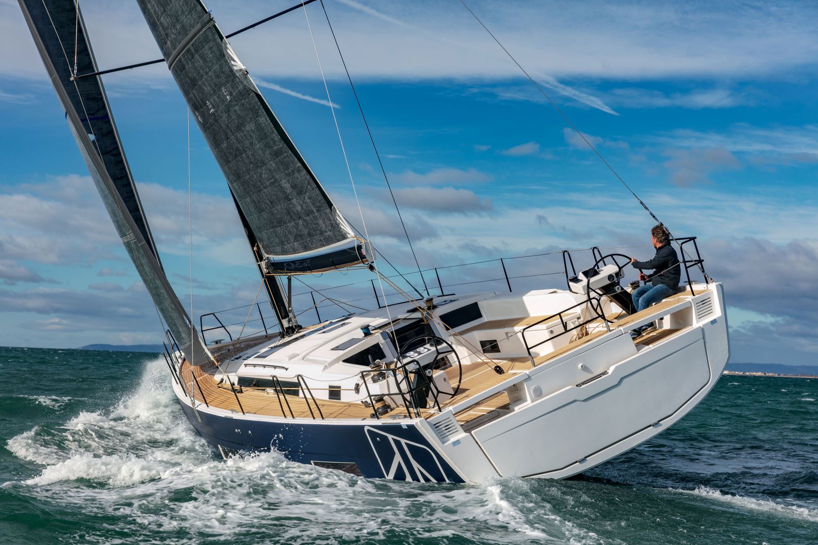 Ein modernes Segelboot mit eleganten schwarzen Segeln, das zum Yachtcharter zur Verfügung steht, kreuzt auf dem Meer. Das Schiff ist leicht nach links geneigt, während es durch das Wasser gleitet und weiße, schaumige Wellen erzeugt. Eine Person steuert das Boot und der Himmel ist teilweise bewölkt und weist Blautöne auf.